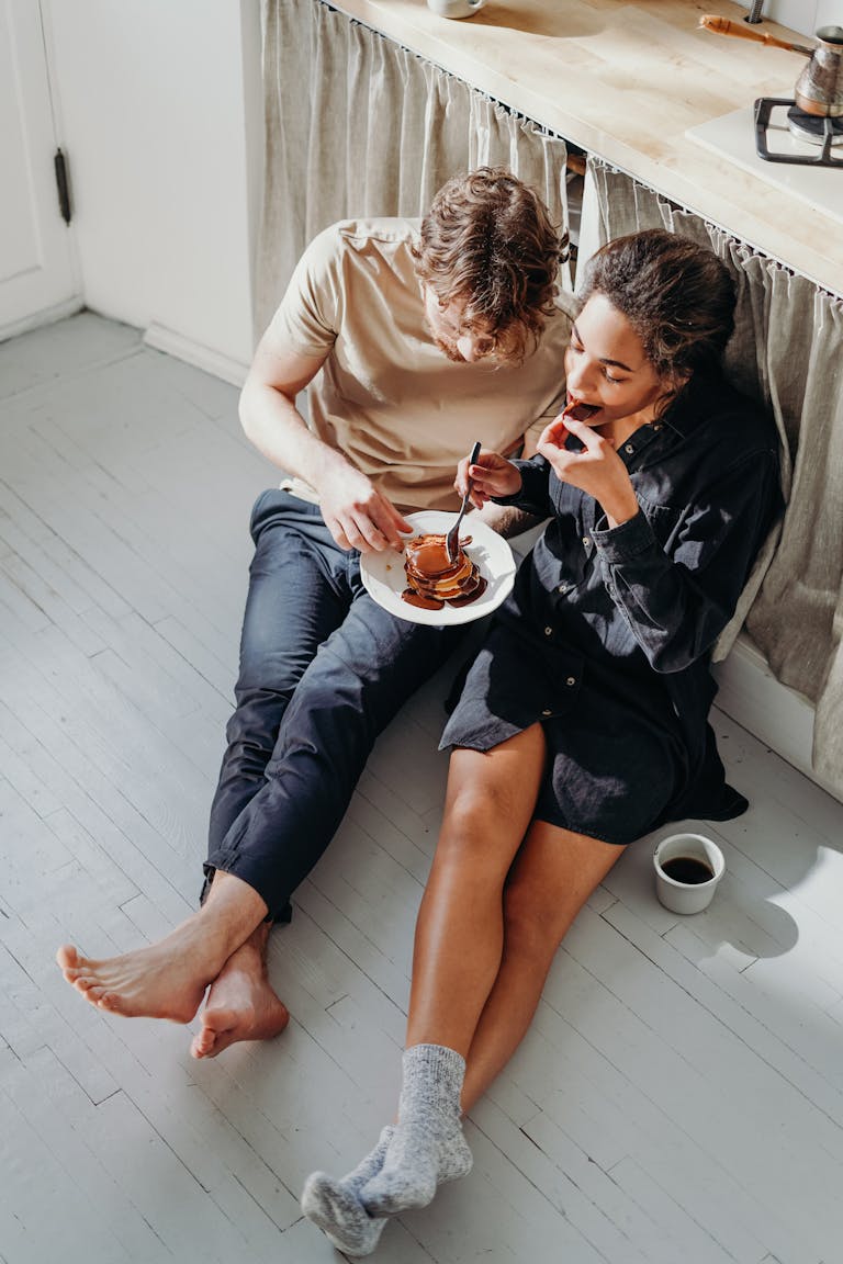 A couple enjoying breakfast together, seated on the floor with pancakes and coffee.
