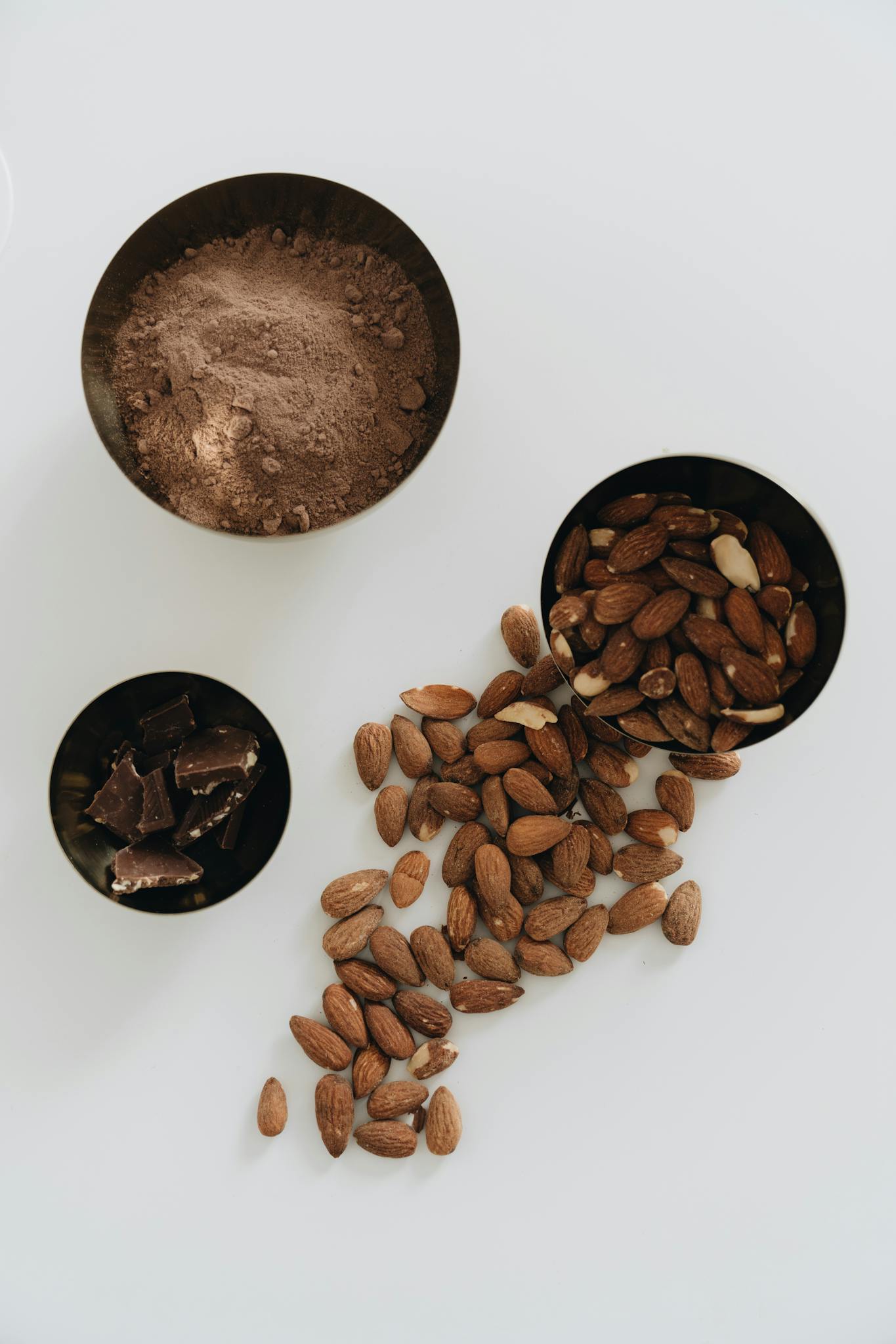 A still life of almonds and dark chocolate with cocoa powder on a white background.