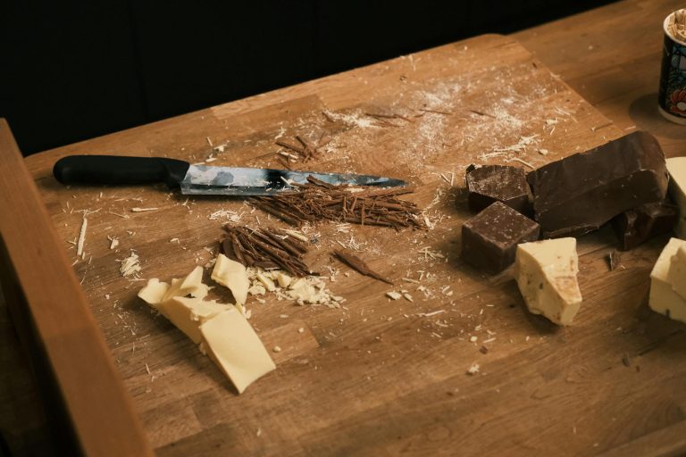 Assorted chocolate blocks and shavings on a wooden cutting board with knife, creating a gourmet scene.