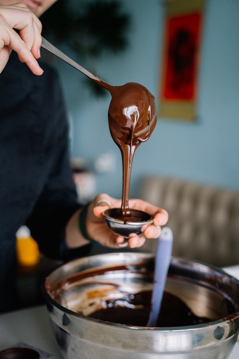 Close-up of chocolate ganache pouring into a container, showcasing culinary detail.