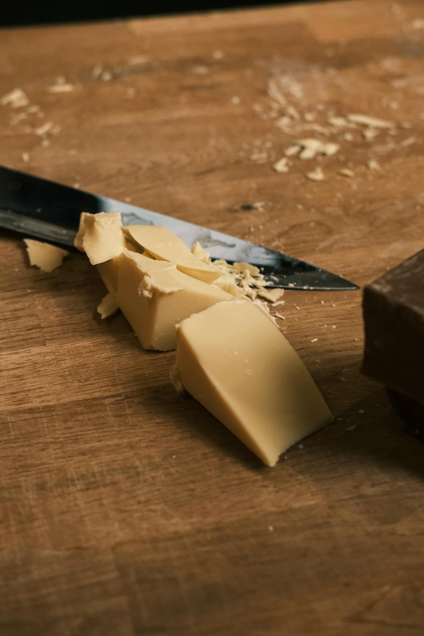 Close-up of chopped white and dark chocolate on a wooden board with a knife.