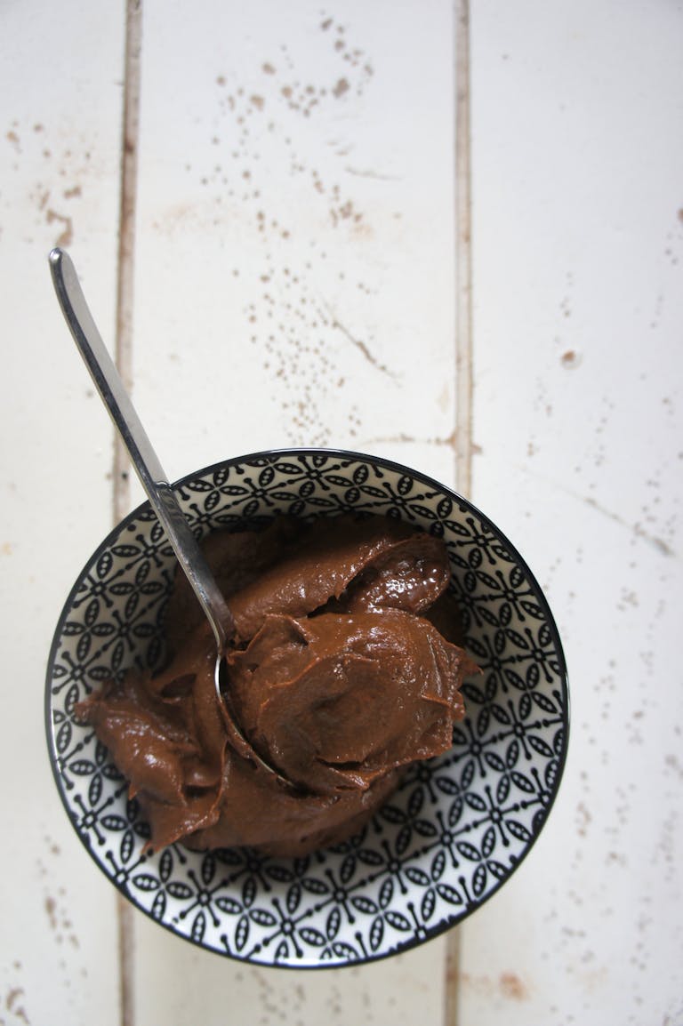 Spoonful of rich chocolate dessert in a patterned bowl on rustic surface.