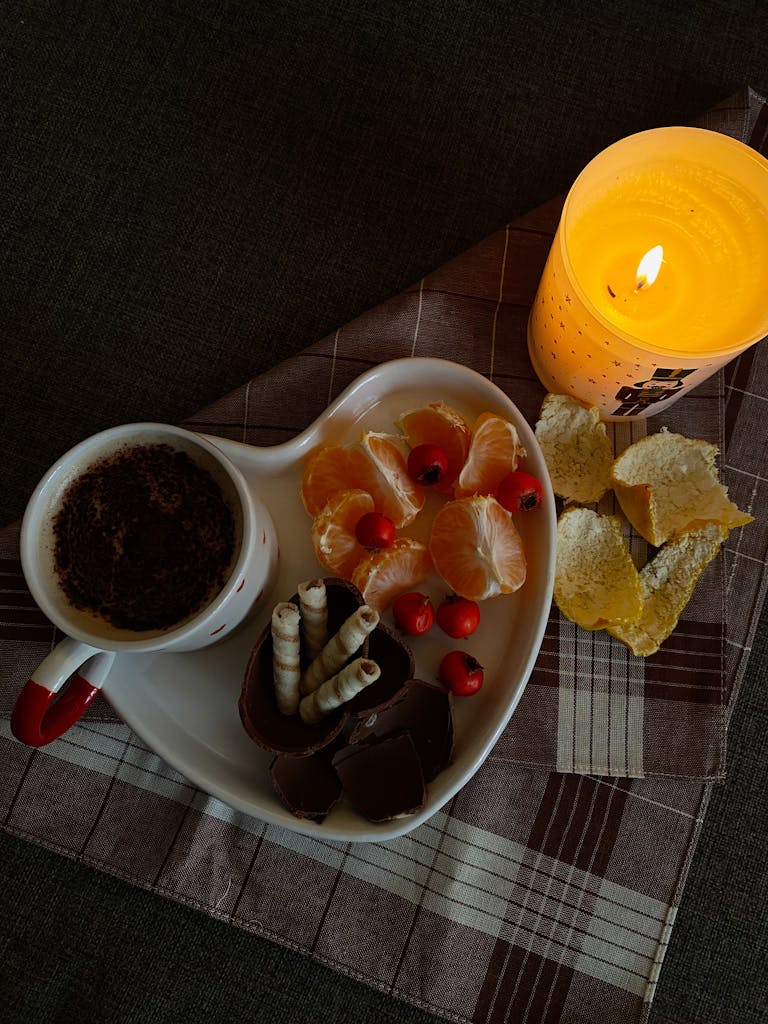 Warm candlelit setting with coffee, chocolate, and fruits on a plaid cloth.